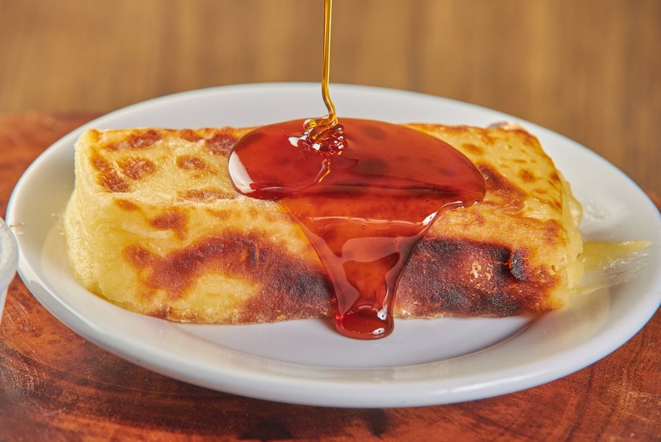 Cartola: banana com queijo coalho num prato branco, recebendo um fio de calda de canela.
