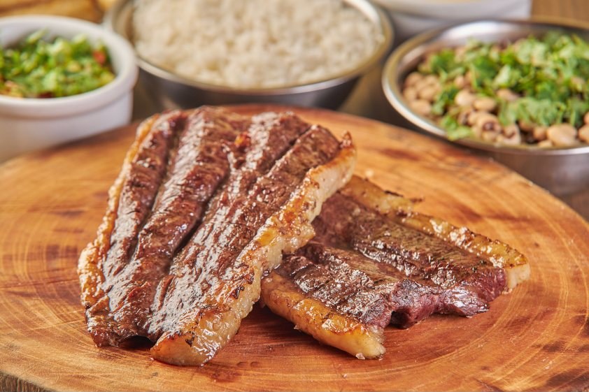 Fatias grossas de carne de sol numa tábua de madeira, acompanhadas de arroz, feijão verde e vinagrete.